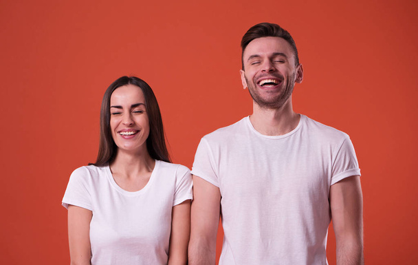 Beautiful young couple in white blank t-shirts are posing on orange background. Relationship, family, advertising - Fotografie, Obrázek