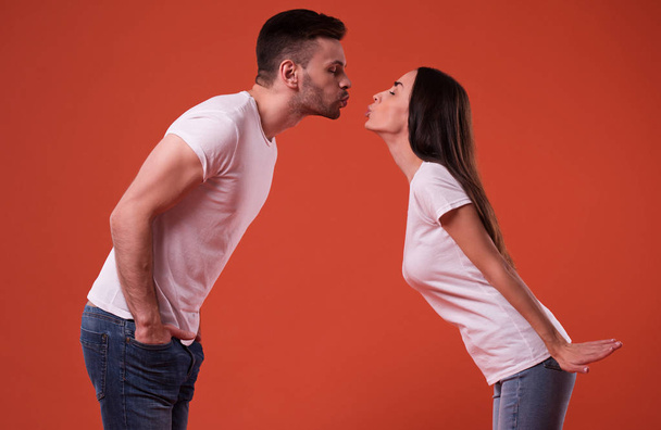 Happy beautiful young couple in love have a fun in white t-shirts while posing on orange background - Photo, image