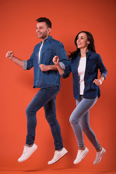Retrato de larga duración de una alegre y excitada pareja joven saltando juntos y celebrando el éxito mientras corre aislada en el estudio
 - Foto, Imagen