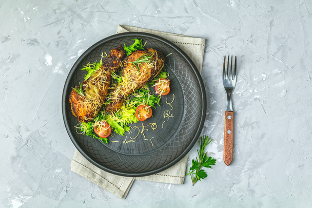 Baked chicken drumstick in a black ceramic plate with orange and rosemary, light gray stone concrete surface, top view, copy space. - Photo, Image