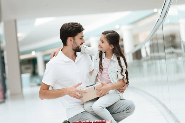 Daughter is sitting on father's lap in shopping mall. Dad and girl are smiling. - Foto, imagen