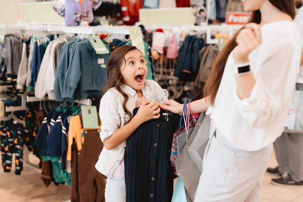 Moeder en dochter in winkelcentrum. Meisje is enthousiast over de nieuwe trui. - Foto, afbeelding