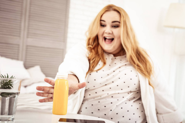 Laughing long-haired ginger woman being happy with bottle of juice - Foto, Imagem