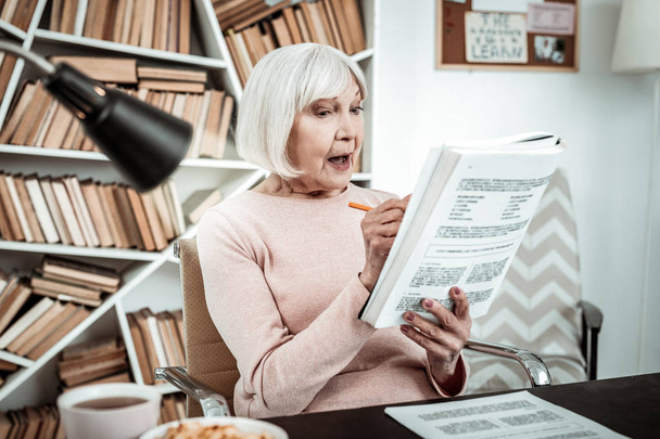 Emotional blonde pensioner making notes in book - Valokuva, kuva