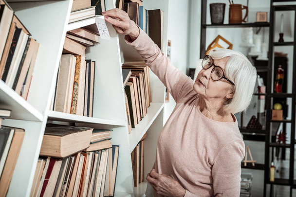 Serious elderly woman putting sticker on shelf - Фото, зображення