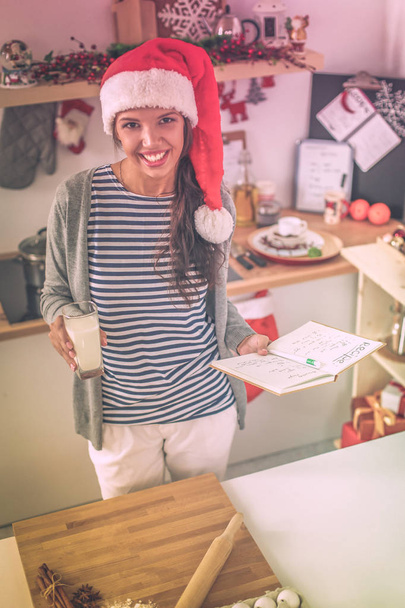 Happy young woman smiling happy having fun with Christmas preparations wearing Santa hat - Photo, Image