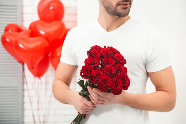 close up of man holding bouquet of red roses with balloons on the background in the room, valentines day concept - Foto, Imagem
