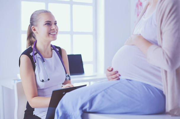 Young woman doctor with stethoscope and tablet speaking with pregnant woman at hospital. - Foto, imagen