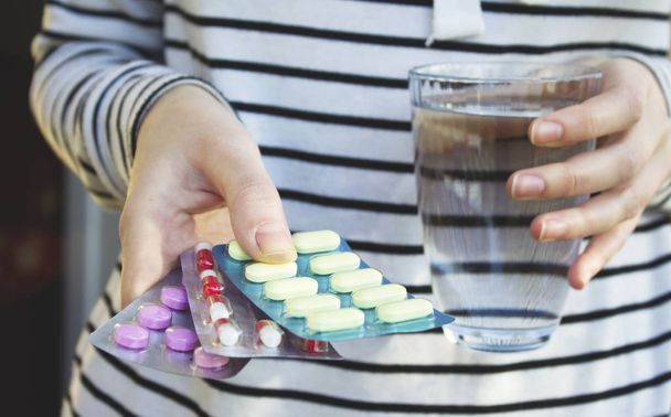 Женщина держит в руках цветные таблетки и стакан воды. Концепция здоровья
. - Фото, изображение