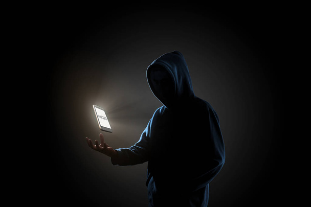 Λευκό smartphone με κείμενο «Χάκερ» στην οθόνη αιωρούμενη παραπάνω hacker του χεριού σε σκούρο φόντο. Οικονομικών, business, e-commerce ή cyber έγκλημα πρωτότ - Φωτογραφία, εικόνα