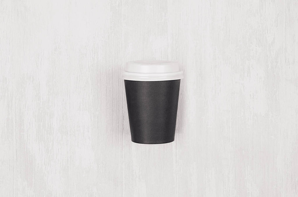 Coffee mockup - blank black paper cup with white cap on white wood board, top view. Modern elegant concept for branding identity, advertising, design. - 写真・画像
