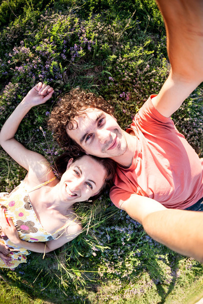 Een man en een vrouw liggen op het gras. Selfies van twee geliefden. Glimlachend paar is samen gefotografeerd. De jongen en het meisje in de weide lopen. - Foto, afbeelding