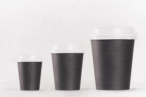 Coffee mockup - set of three different size blank black paper cups with white cap on white wood table, coffee shop interior. Modern elegant concept for branding identity, advertising, design. - Fotoğraf, Görsel