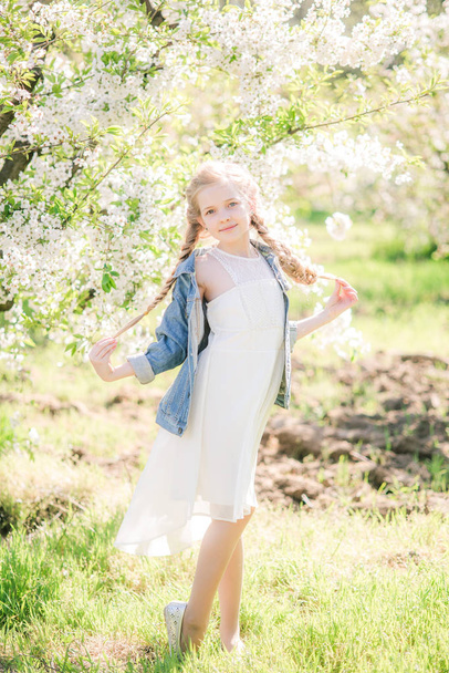 Cute girl with blond hair in a white sundress in spring in a lush garden - Foto, Bild