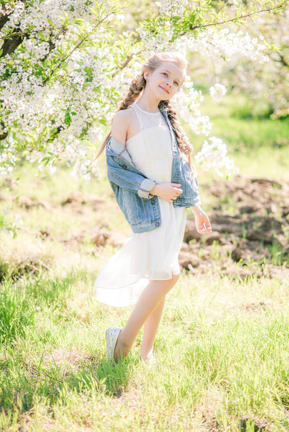Cute girl with blond hair in a white sundress in spring in a lush garden - 写真・画像