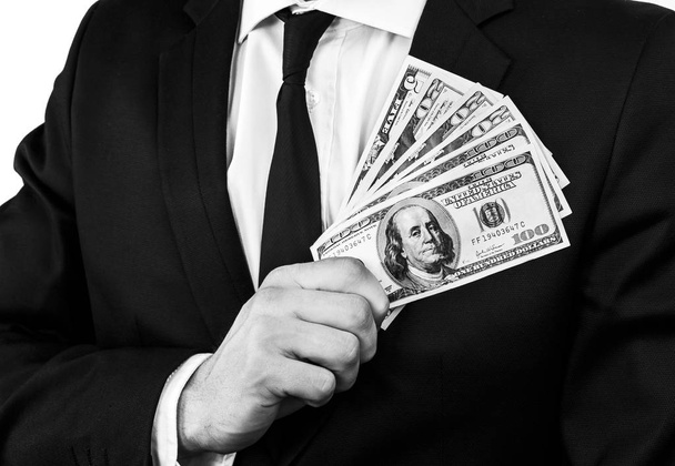 Black and white image of a young man in a black suit holding a certain amount of American dollar banknotes - Φωτογραφία, εικόνα