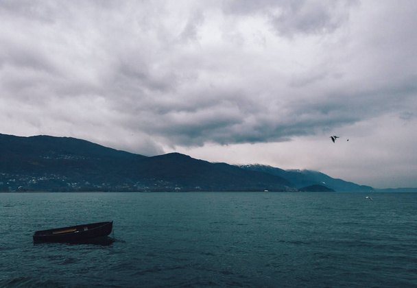 Eenzame houten boot in Ohrid Lake op een bewolkte dag - Foto, afbeelding