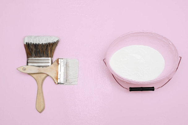 Two paint brushes, next to a bucket lie on a textured white surface - Foto, afbeelding