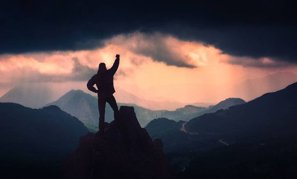 Wanderer, der mit erhobener Hand den Gipfel des auf einer Felswand stehenden Berges bezwang. - Foto, Bild