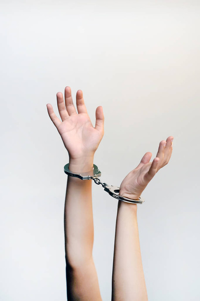 逮捕された女性の手に手錠をかけました。囚人や逮捕されたテロリスト、茶色の背景に分離されて手錠で手のクローズ アップ。刑事の女性の手は、手錠でロックされています。クローズ アップ ビュー. - 写真・画像