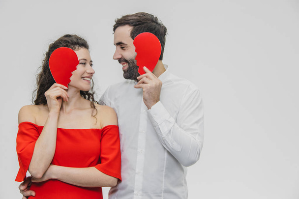 Portrait of a Loving Young Couple. A man is dressed in a white shirt, his wife in a red dress. Conducting two parts of the heart paper. - Foto, Imagem