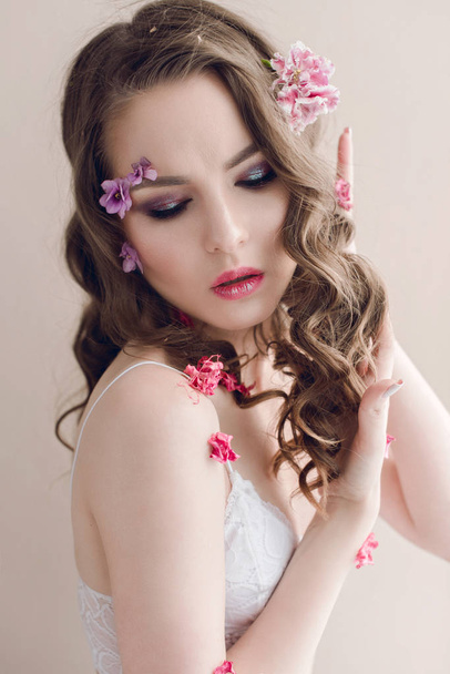 Cosméticos y manicura. Retrato de cerca de una mujer atractiva con flores secas en su cara, color pastel, maquillaje perfecto y piel. Retrato retocado de primavera fresco, moderno
 - Foto, imagen