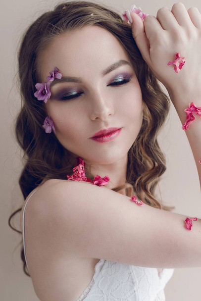 Cosmetics and manicure. Close-up portrait of attractive woman with dry flowers on her face, pastel color, perfect make-up and skin. Fresh, trendy, spring retouched portrait - Photo, Image