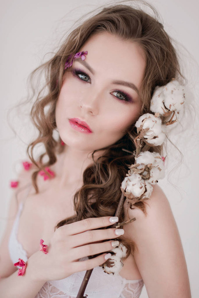 Cosmetics and manicure. Close-up portrait of attractive woman with dry flowers on her face, pastel color, perfect make-up and skin. Fresh, trendy, spring retouched portrait - Foto, imagen