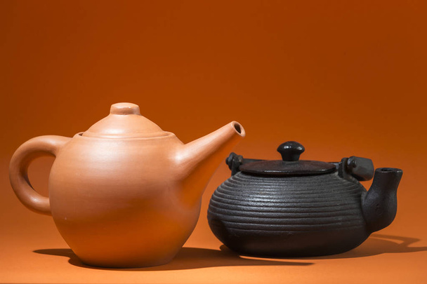 Teekanne aus Ton und Teekanne aus Eisen in verschiedenen Formen auf orangefarbenem Hintergrund - Foto, Bild