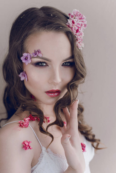 Cosméticos y manicura. Retrato de cerca de una mujer atractiva con flores secas en su cara, color pastel, maquillaje perfecto y piel. Retrato retocado de primavera fresco, moderno
 - Foto, Imagen