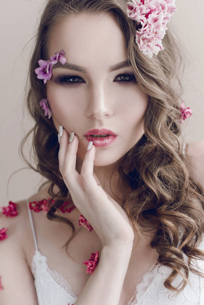 Cosmetics and manicure. Close-up portrait of attractive woman with dry flowers on her face, pastel color, perfect make-up and skin. Fresh, trendy, spring retouched portrait - Фото, изображение