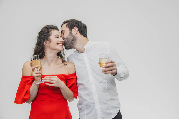 Loving young couple drinks champagne. On a white background. Dressed in red dress and white shirt. - Фото, зображення