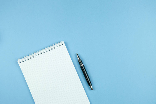 Kockás notebook a fehér papír és toll kék háttér. - Fotó, kép
