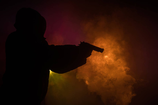 Silhouette of man with pistol ready to attack on dark toned foggy background or dangerous bandit holding gun in hand. Shooting terrorist with weapon theme decor - Foto, Bild