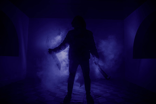 危険なフード男は暗闇の中で立っていると、大きなナイフを保持しています。顔を見ていないことができます。犯罪概念をコミット - 写真・画像