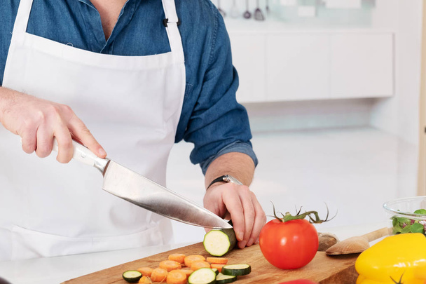 Hombre cortando verduras de pie en su cocina preparando plato vegano
 - Foto, imagen