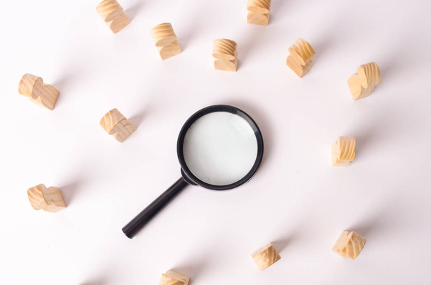 Wooden figures of people lie around a magnifying glass on a white background. Hiring for work, tracing people. The concept of the search for people and workers, human resources. - Fotoğraf, Görsel