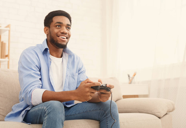 Emotional african-american guy playing video game with joystick at home, copy space - Foto, afbeelding