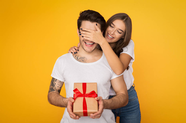 Chica cubriendo ojos de novio y dándole regalo
 - Foto, imagen