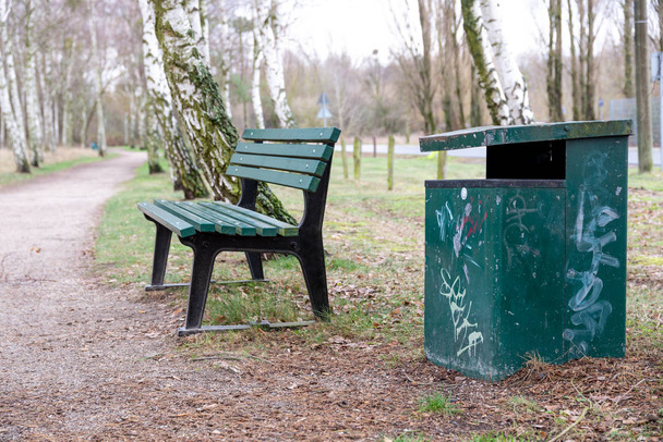 Um banco de parque verde com lata de lixo no parque no meio entre bétulas
 - Foto, Imagem
