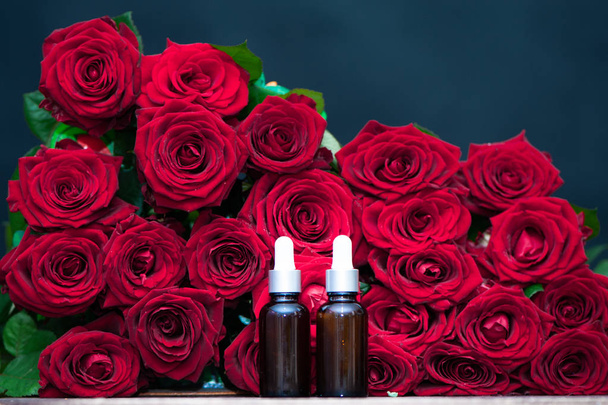 Το έλαιο τριαντάφυλλου, μπουκάλια και φρέσκα λουλούδια και φύλλα σε ένα φυσικό υπόβαθρο, βιο, οργανικά, φύση καλλυντικά έννοια - Φωτογραφία, εικόνα