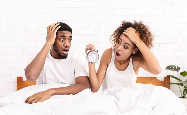 Nukkumassa. Nuori afrikkalais-amerikkalainen pari jäi soimaan herätyskelloa ja ovat myöhässä, istuu sängyssä, panoraama, kopioi tilaa
 - Valokuva, kuva