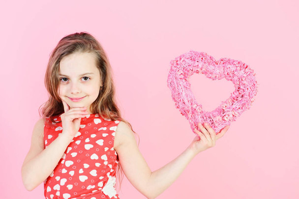 Valentine and valentines day celebration. Happy girl holding rosy heart on pink background. Romantic love concept. Sweetheart child with long hair smiling in red dress. Kindness and tenderness - Photo, image