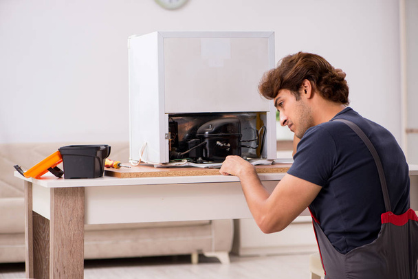 Молодой красивый подрядчик ремонтирует холодильник
  - Фото, изображение