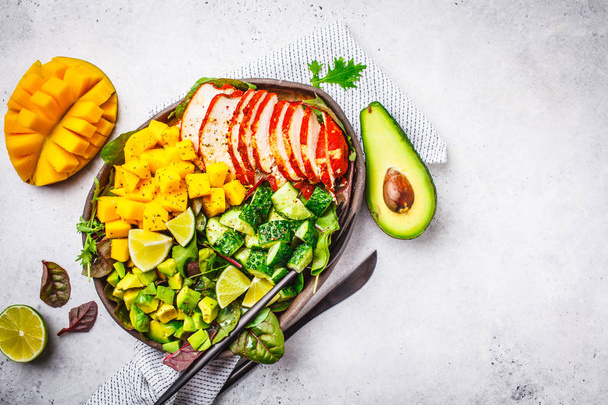 Grilled chicken, mango and avocado salad in a dark dish on white background. - Фото, изображение