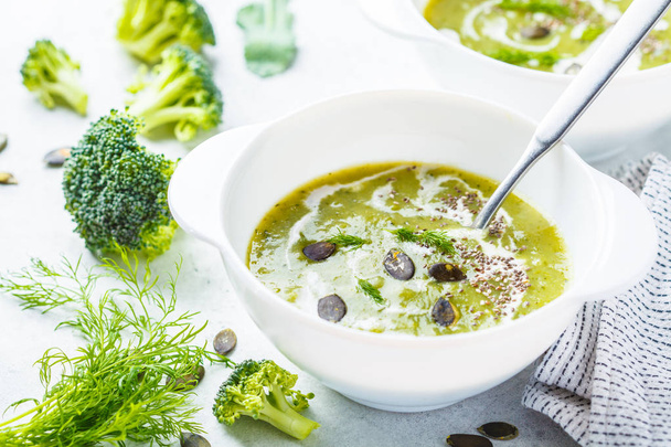 Vegan detox broccoli cream soup with coconut cream and pumpkin seeds in a white bowl. Plant based food concept. - Fotoğraf, Görsel