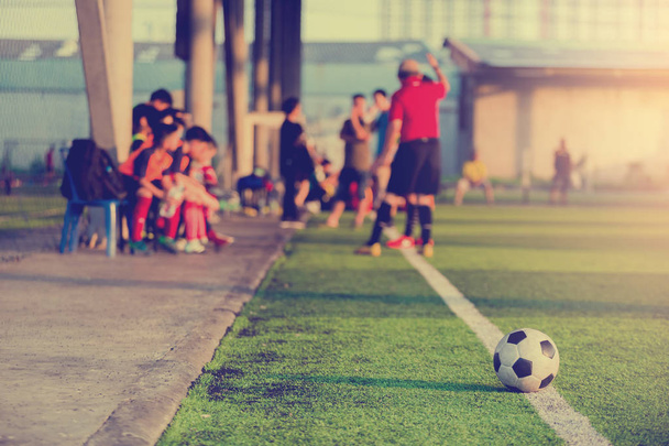 μπάλα ποδοσφαίρου στο touchlines σχετικά με τεχνητό χλοοτάπητα με θολή ποδόσφαιρο παίκτες και προπονητής προπόνηση στο παιχνίδι. - Φωτογραφία, εικόνα