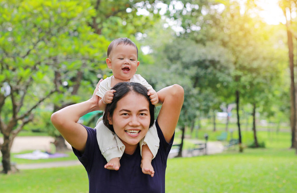 Beautiful young Asian mother with happy baby boy riding on mom's shoulder in the nature park. - Foto, Imagem
