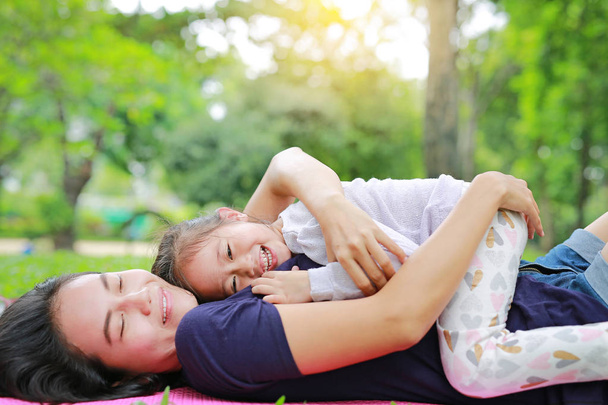 Bonne maman asiatique embrasser sa fille couchée dans la pelouse verte. Mère drôle et fille enfant jouant dans le parc d'été
. - Photo, image