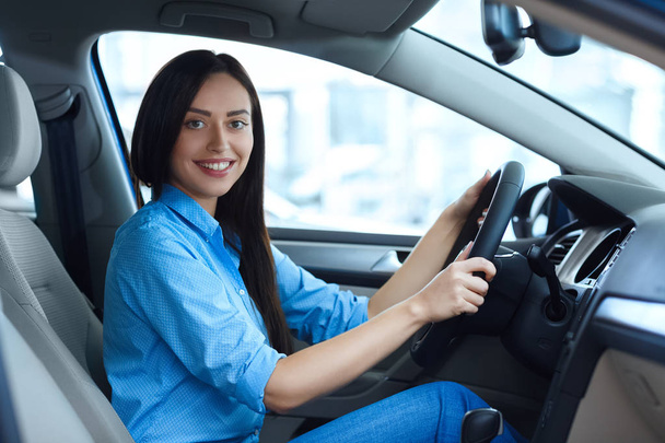 Gotowy do drogi. Piękna młoda kobieta uśmiechając się szczęśliwie do kamery, siedząc w nowy samochód w salonie samochód - Zdjęcie, obraz